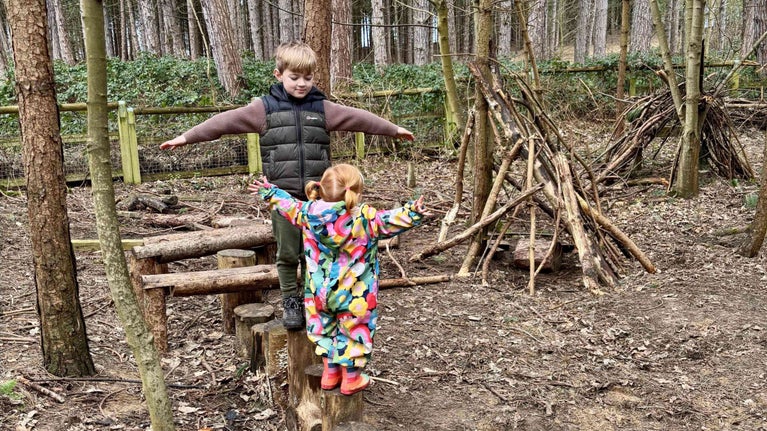 Two young children balancing on tree stumps at the Formby Kirklake natural playtrail in the woodlands